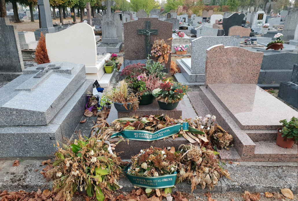 Tombeau dans un cimetière avec des bouquets fanés et corbeilles de fleurs, tombes voisines en granit et pierre.
