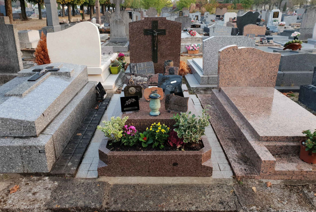 Tombeau de cimetière bien entretenu avec fleurs et monuments en pierre, décorations et gravures au milieu des tombes.