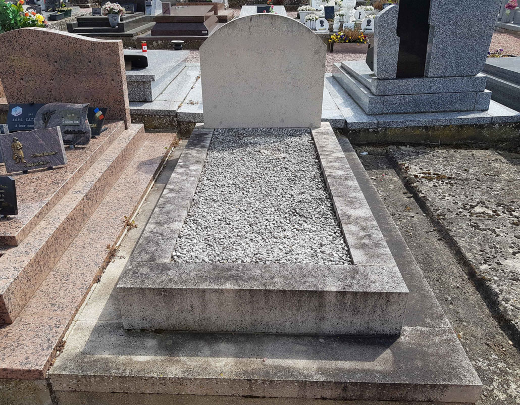 Tombe grave rectangulaire en pierre avec dalle gravillonnée, entourée de dalles, dans un cimetière.
