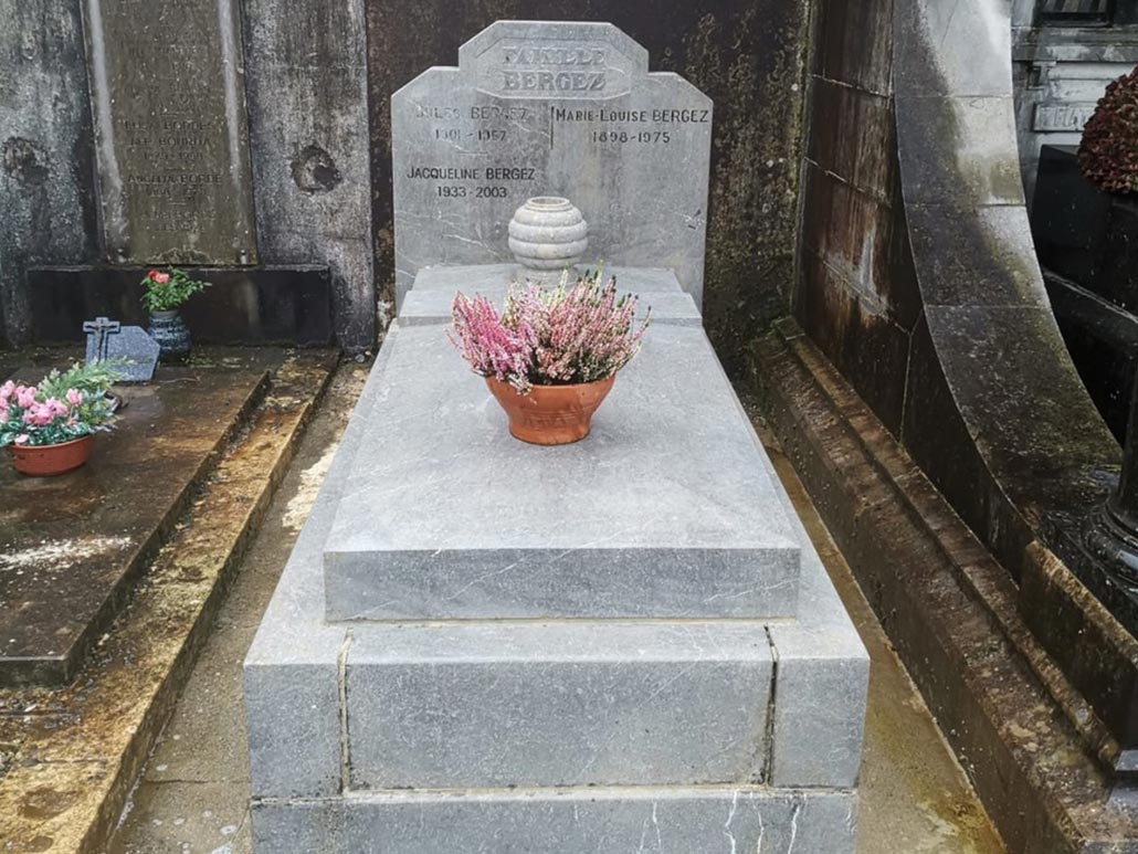 Tombe en pierre grise orientée longitudinalement, vase fleurs au centre et pierres tombales gravées à l’arrière.
