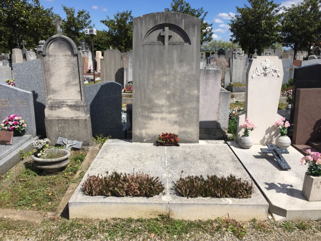 Tombe simple au cimetière, pierre grise avec arc et croix sculptée, tombeau divisé en deux sections, bouquets et fleurs